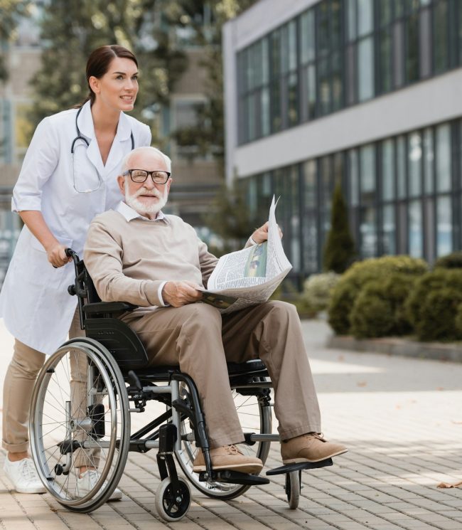geriatric nurse walking with elderly disabled man in wheelchair with newspaper outdoors geriatric nurse walking with elderly disabled man in wheelchair with newspaper outdoors